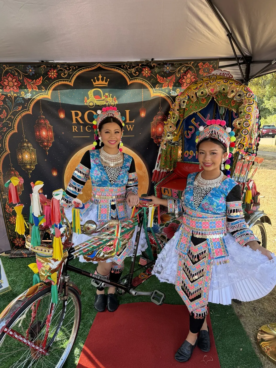 Two young performers in blue costumes posing beside the rickshaw